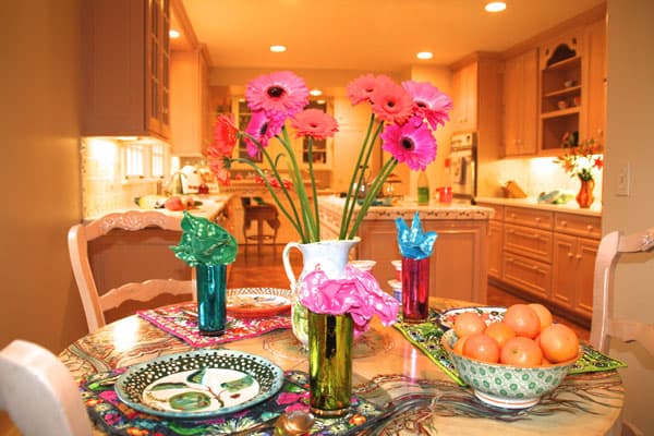 Join us for lunch! The vibrant colors of the Gerbera daisies, tangerines, reflective drinking glasses, patterned placemats and handmade ceramic plates bring joy to an otherwise neutral kitchen.